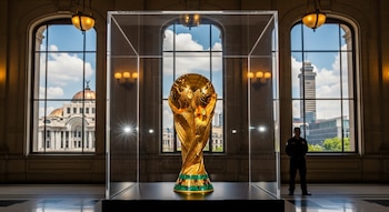 El Trofeo de la Copa Mundial de la FIFA en vitrina de cristal. Detrás, por ventanales, se observa el Palacio de Bellas Artes y un guardia de seguridad.