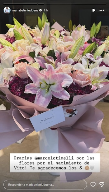 Un gran ramo de flores frescas en tonos rosa claro, blanco y morado, envuelto en papel rosa pálido, con una tarjeta que dice "M. BELEN"