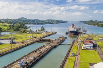 Vista aérea de las esclusas del Canal de Panamá con un barco carguero, remolcadores, vías de ferrocarril y vegetación.