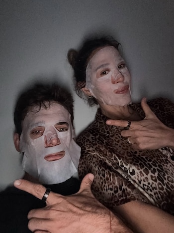 Jimena Barón y Matías Palleiro, con mascarillas faciales blancas, posan para una selfie. Ella con blusa de leopardo, él con camiseta oscura. Ambos señalan con el pulgar
