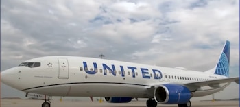 Un avión comercial de colores blanco y azul con el nombre United, detenido sobre el asfalto de un aeropuerto bajo un cielo con nubes