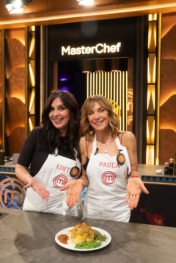 Edith Hermida y Paula Trapani con delantales blancos señalan un plato servido sobre un mostrador en un estudio de televisión