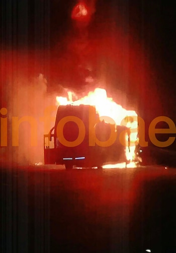 Un micro de pasajeros se incendia con grandes llamas y denso humo en una ruta oscura de noche. El logotipo de Infobae se superpone en la imagen