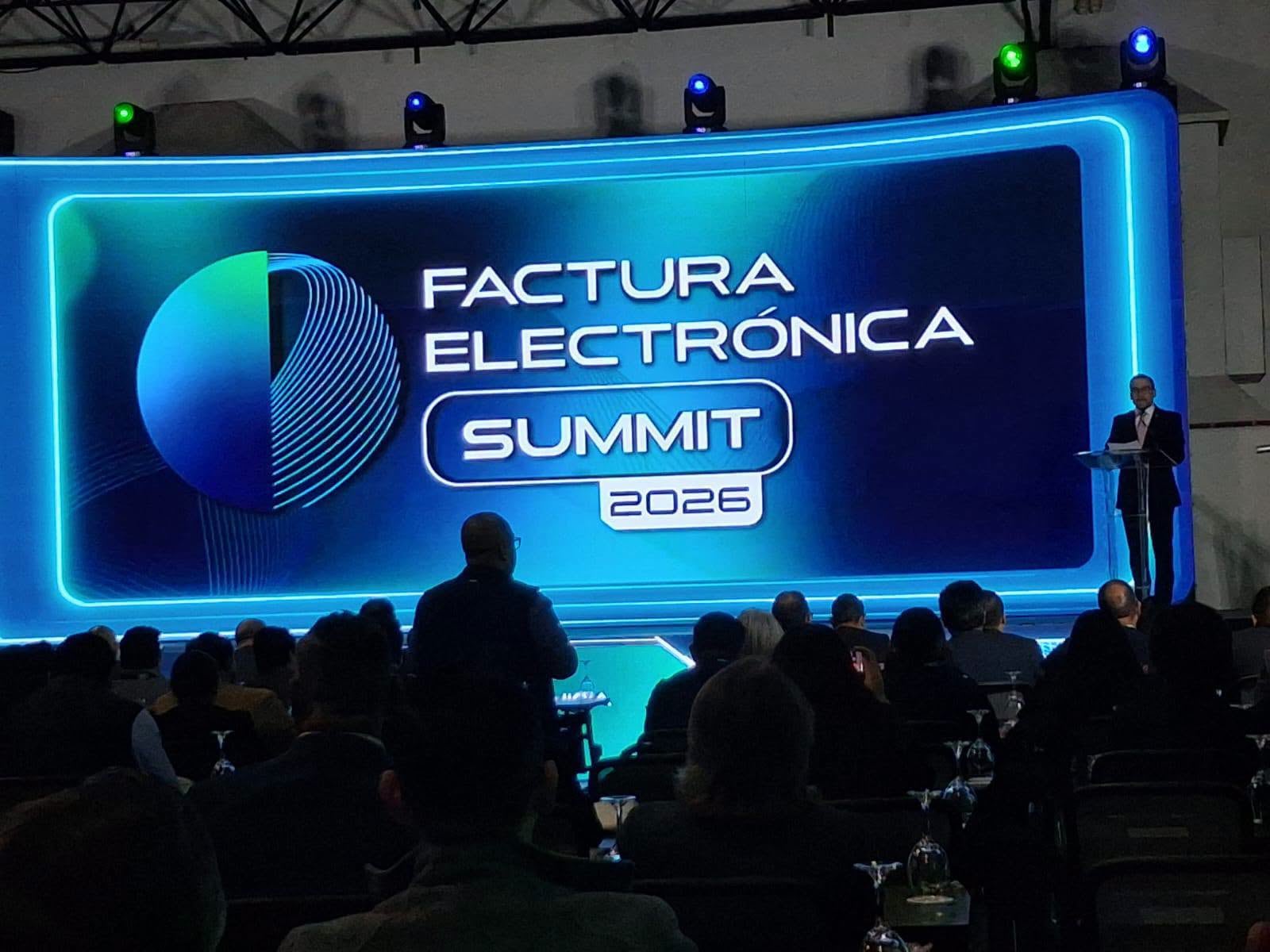 Un ponente dirige una conferencia ante los asistentes frente a una pantalla con la inscripción Factura Electrónica Summit 2026. (Román Castro, FEL SUMMIT 2026)