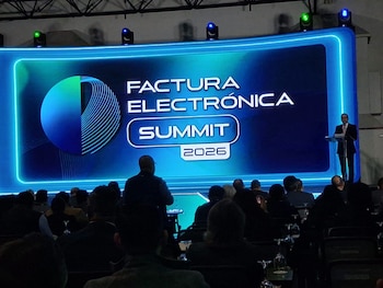 Un hombre en traje habla desde un atril junto a una pantalla azul que dice Factura Electrónica Summit 2026 frente a un público sentado