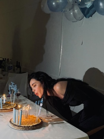 Priscila Crivocapich, con cabello oscuro y un vestido negro, se inclina para soplar las velas de un pastel de cumpleaños sobre una mesa blanca