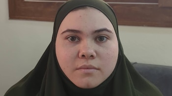 Primer plano de una mujer joven con un hiyab de color verde oliva sobre un fondo de pared clara y marco de madera