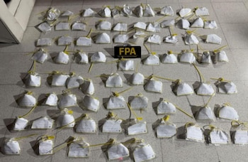 Múltiples paquetes individuales blancos sellados con precintos amarillos dispuestos sobre un suelo de baldosas. Una placa negra con las letras FPA en amarillo en el centro