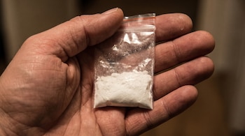 Una mano abierta sosteniendo una pequeña bolsa de plástico transparente con cierre de cremallera, que contiene una cantidad de polvo blanco.