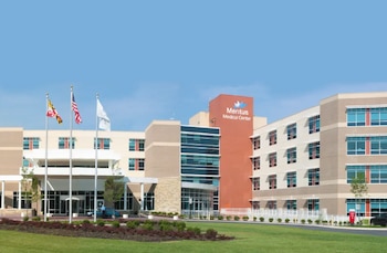 Edificio del Meritus Medical Center con fachadas beige y rojiza. Césped, arbustos, tres mástiles con las banderas de Maryland, Estados Unidos y una blanca
