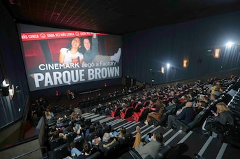 Interior de una sala de cine con una gran pantalla que muestra un anuncio de Cinemark y una audiencia sentada en las butacas oscuras