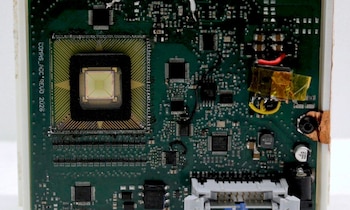 Placa de circuito impreso verde con un sensor cuadrado montado, microchips, cables y diversos componentes electrónicos