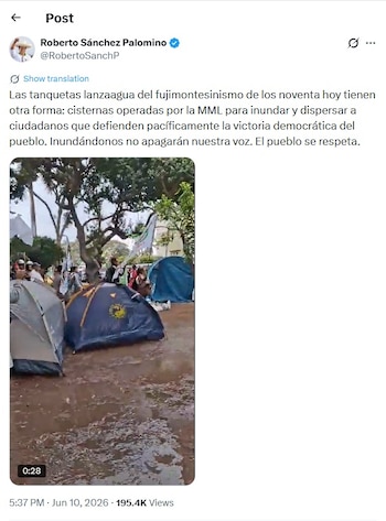 Múltiples tiendas de campaña en un terreno inundado y embarrado, con árboles y personas manifestándose en el fondo