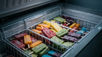 Varias paletas heladas de diversos colores dentro de canastillas metálicas en un congelador cubierto de escarcha.