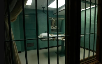 Una camilla médica con correas de sujeción dentro de una habitación de paredes verdes, vista a través de varios barrotes