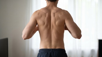 Vista trasera de una persona sin camisa con la espalda expuesta, mostrando los codos retraídos y las escápulas apretadas. La piel es clara y los músculos están definidos.