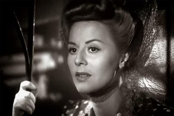 Retrato en blanco y negro de Aída Luz, una mujer con peinado elegante y maquillaje, mirando hacia la derecha mientras sostiene un objeto fino y oscuro con su mano izquierda