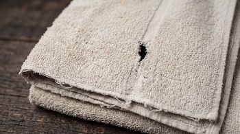 Primer plano de dos toallas beige dobladas y desgastadas con un pequeño orificio en la tela sobre una mesa de madera oscura.