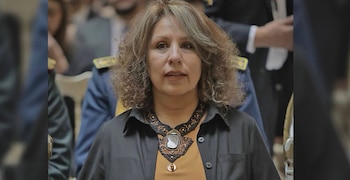 Primer plano de Cinthia Yáñez, mujer con cabello rizado y tez clara, vestida con una camisa oscura, un suéter naranja y un collar elaborado