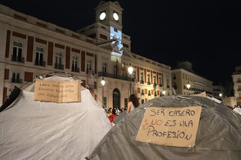 Tiendas de campaña situadas de noche en una plaza frente a un edificio oficial, con carteles de cartón escritos a mano