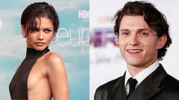 Zendaya en primer plano a la izquierda, cabello oscuro, vestido negro con cuello alto. A la derecha, Tom Holland sonríe en primer plano con traje oscuro y camisa blanca