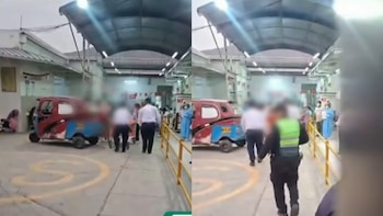 Una mototaxi roja y azul estacionada en el ingreso a un hospital, rodeada de personas, personal de salud y un policía