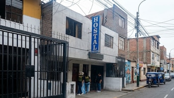 Fachada de un edificio con un letrero vertical de hostal y agentes de la policía en la entrada frente a una calle con vehículos
