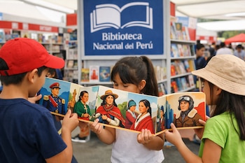 Tres niños observan un libro desplegable tipo acordeón con ilustraciones. Al fondo, un cartel azul de la Biblioteca Nacional del Perú y estantes con libros.