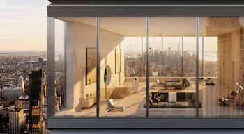 Vista interior de un espacio moderno con ventanales de piso a techo y vistas al horizonte de una ciudad al atardecer, con muebles contemporáneos y una persona en un sofá