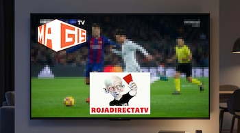 Un televisor smart montado en una pared muestra un partido de fútbol borroso. En la pantalla, se ven los logos de Magis TV y RojaDirecta TV.