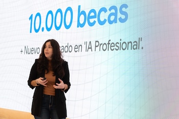Una mujer de cabello oscuro presenta frente a una gran pantalla que muestra el texto "10.000 becas" y "Nuevo grado en 'IA Profesional'"