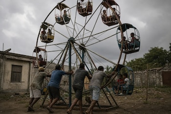 Cuatro hombres empujan la estructura metálica de una rueda de la fortuna que transporta a varios niños en sus cabinas.
