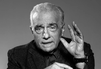 Imagen en blanco y negro del director Martin Scorsese, un hombre mayor de cabello blanco, con una chaqueta tweed, gesticulando con su mano derecha abierta y elevada