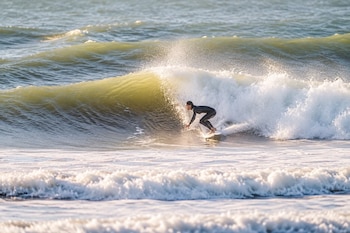 Una persona con traje de neopreno negro navega sobre una tabla de surf en la cresta de una ola