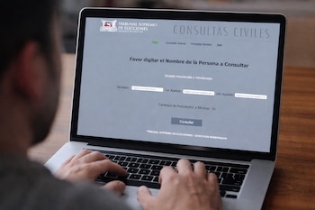 Persona tecleando en un ordenador portátil; la pantalla muestra el sitio web del Tribunal Supremo de Elecciones de Costa Rica con campos de consulta de nombre y apellidos.
