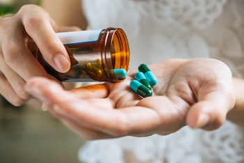 Una mujer vuelca varias pastillas de un frasco sobre su mano (Magnific)