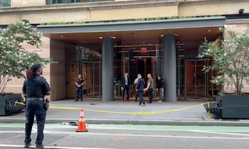 Un oficial de policía observa la entrada de un edificio con columnas de color gris acordonada con una cinta amarilla de precaución
