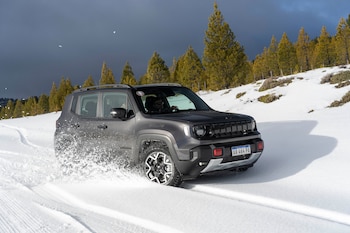 Jeep Renegade de color gris oscuro conduciendo en un camino nevado. Las ruedas levantan nieve. Hay pinos y cielo oscuro al fondo. La matrícula es AA 464 PA