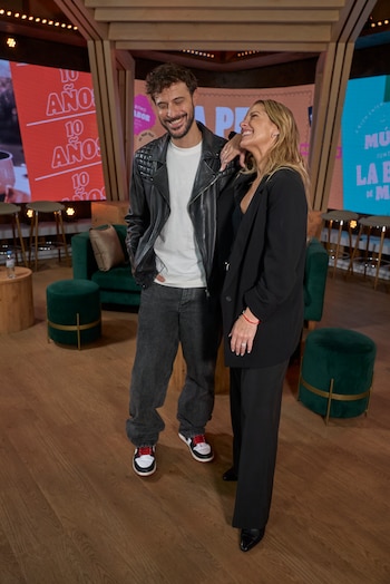 Diego Leuco y Carina Zampini sonríen frente a cámaras en un set de televisión moderno con pantallas coloridas y sillones verdes