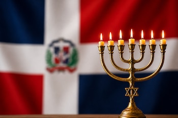 Un candelabro de siete brazos con velas encendidas sobre una mesa de madera frente a la bandera de República Dominicana desenfocada.