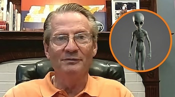 Primer plano de un hombre con gafas y camisa naranja sentado, con una imagen de un alienígena gris con ojos grandes en un círculo naranja superpuesto a la derecha.