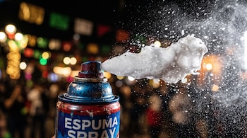 Lata metálica de aerosol etiquetada como ESPUMA SPRAY expulsando espuma blanca y diminutas gotas de líquido.