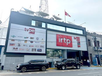 Fachada exterior del edificio del IRTP y TVPerú, con sus logos visibles, una bandera peruana en el techo con antenas parabólicas y dos vehículos negros estacionados