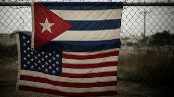 Banderas de Cuba y Estados Unidos colgadas en una reja metálica con alambre de púas
