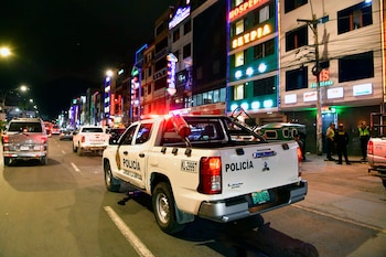 Camionetas policiales blancas y otros vehículos circulan de noche por una avenida frente a edificios comerciales con anuncios luminosos