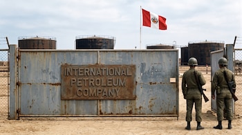 Dos soldados con fusil frente a un portón de metal con el nombre International Petroleum Company, tanques petroleros y una bandera peruana.
