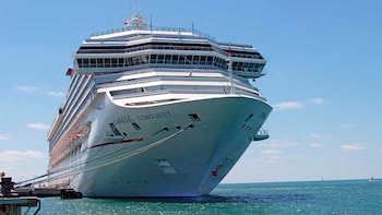 Proa de un gran crucero blanco con el nombre Carnival Conquest amarrado con cuerdas en un muelle sobre el mar