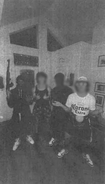 Cuatro personas con los rostros difuminados posan de pie en un interior, mientras una de ellas sostiene un arma larga verticalmente