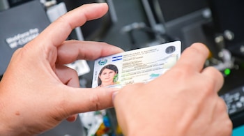 Dos manos sostienen una tarjeta de identificación blanca de El Salvador con bandera, escudo, la foto de una mujer y texto de prueba.