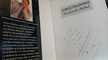 Páginas abiertas de un libro blanco. En la derecha, un autógrafo y dedicatoria manuscrita de Jorge Valdano. A la izquierda, texto biográfico y una foto pequeña de Valdano